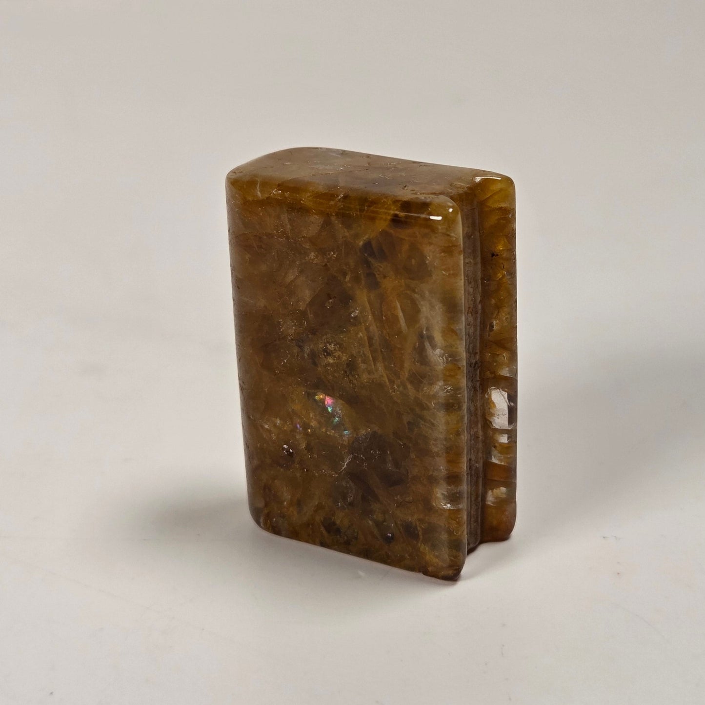A small polished brown stone or crystal block standing upright on a plain light surface.