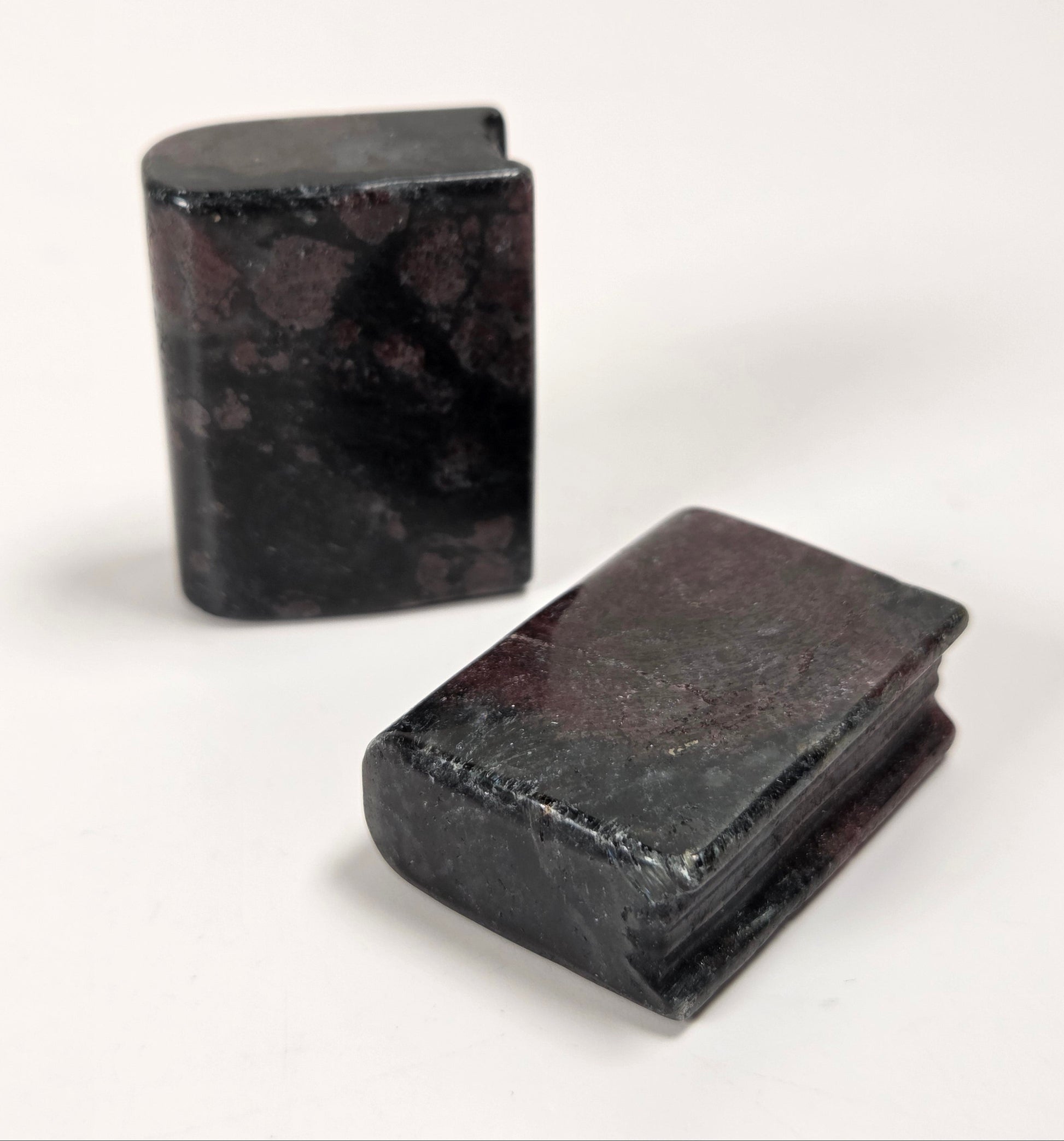 Two small rectangular dark stone objects with a mottled black and reddish-brown marbled pattern, photographed on a plain white background.