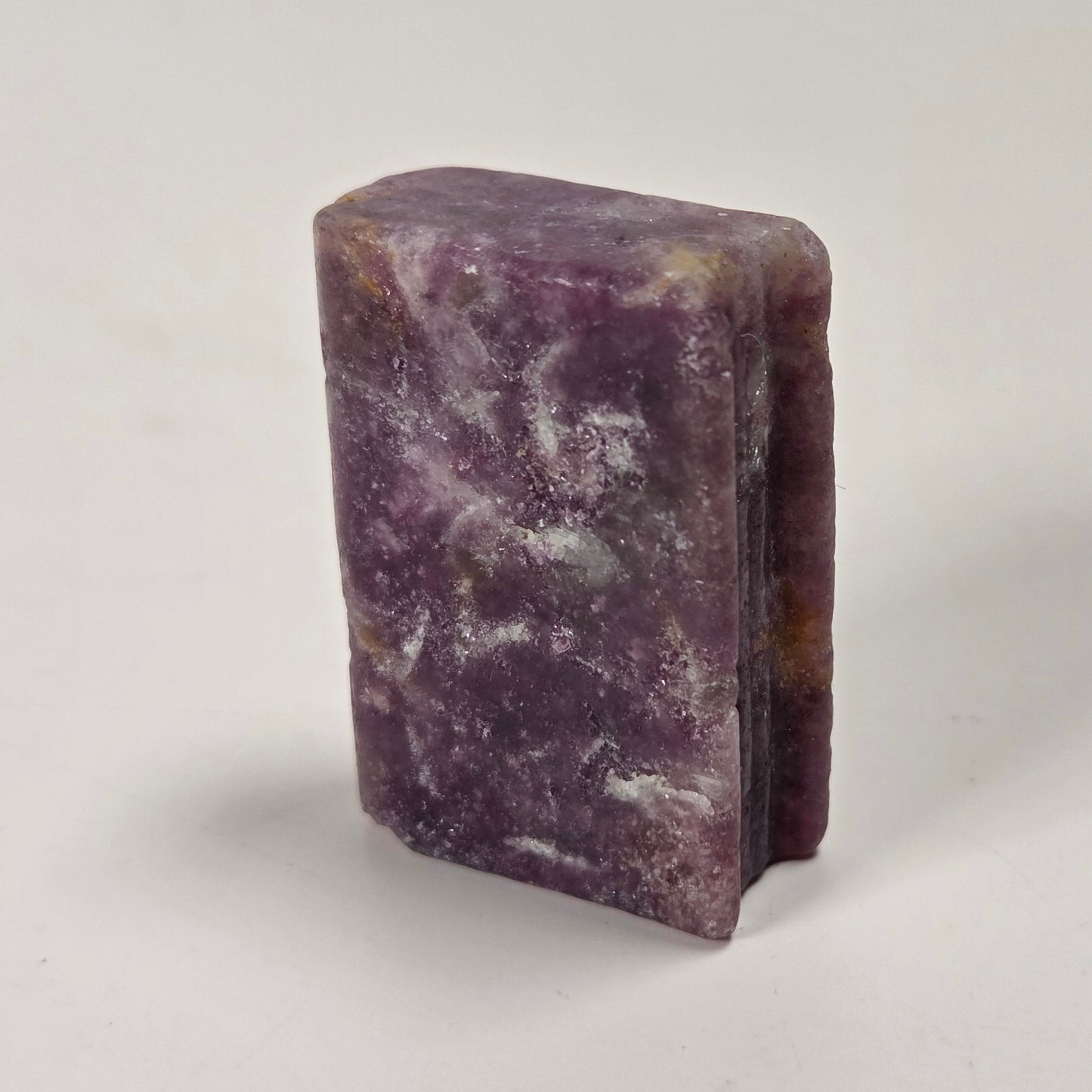 A rectangular purple stone or crystal block with natural marbled patterns, standing upright on a plain light gray surface.