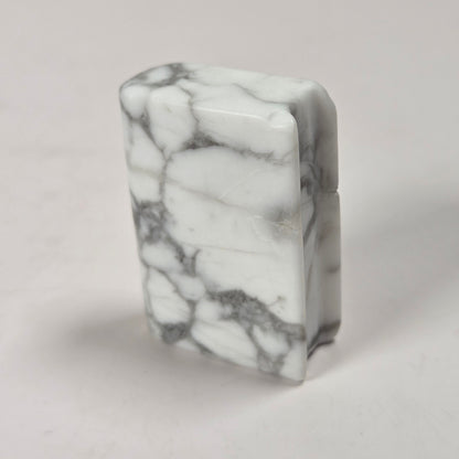 A rectangular lighter made of white marble with prominent gray veining, standing upright on a light gray surface.