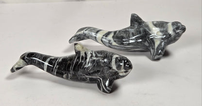 Two polished black and white marbled stone dolphin figurines displayed on a light surface against a marble-patterned background.