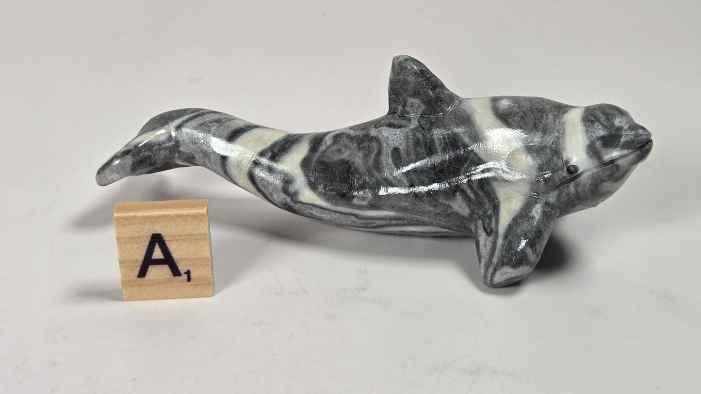 A small polished stone dolphin figurine with a black and white marbled pattern, displayed on a light gray surface next to a wooden letter tile showing the letter 'A'.