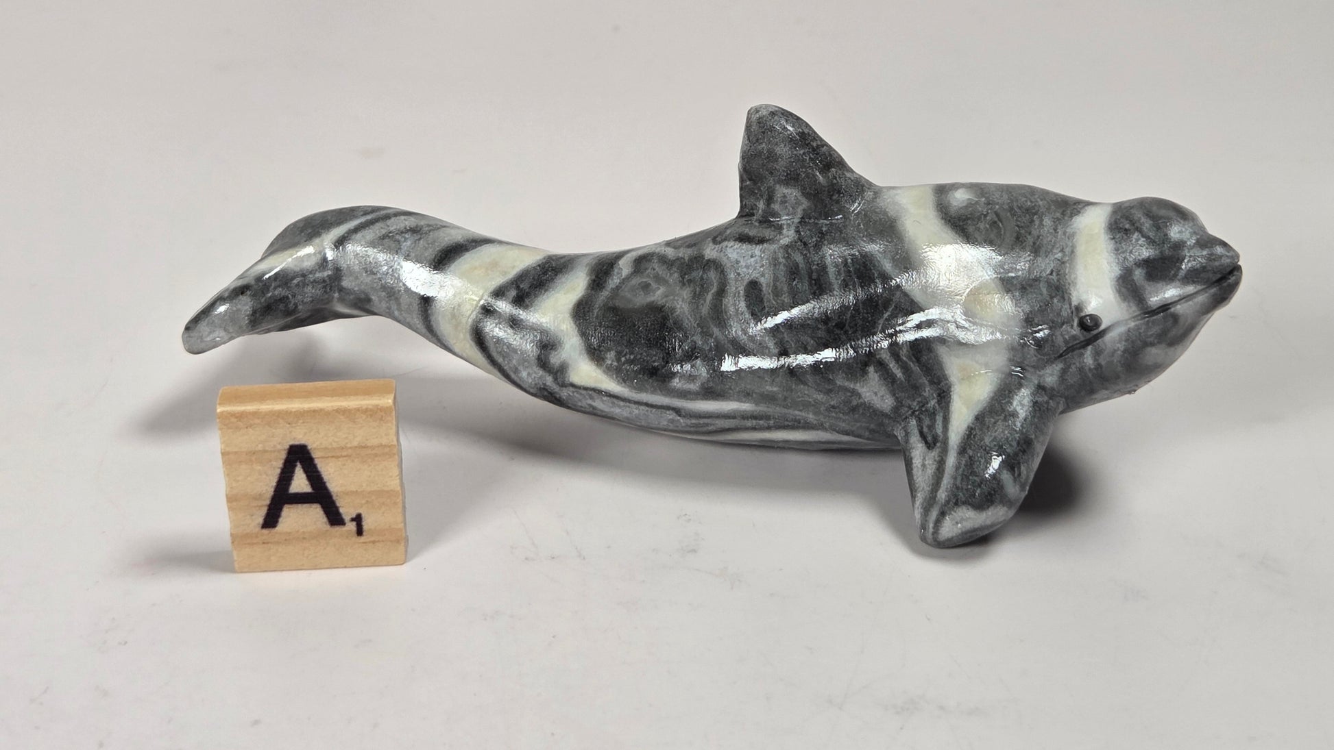 A small polished stone dolphin figurine with a black and white marbled pattern, displayed on a light gray surface next to a wooden letter tile showing the letter 'A'.