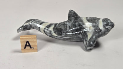 A small polished stone dolphin figurine with a black and white marbled pattern, displayed on a light gray surface next to a wooden letter tile showing the letter 'A'.