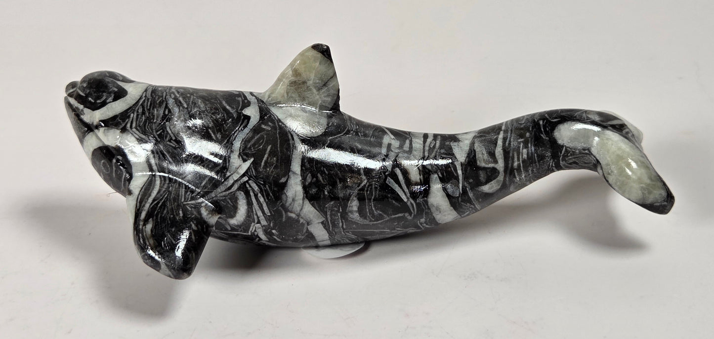 A polished black and white marbled stone dolphin figurine, displayed on a neutral light gray background.