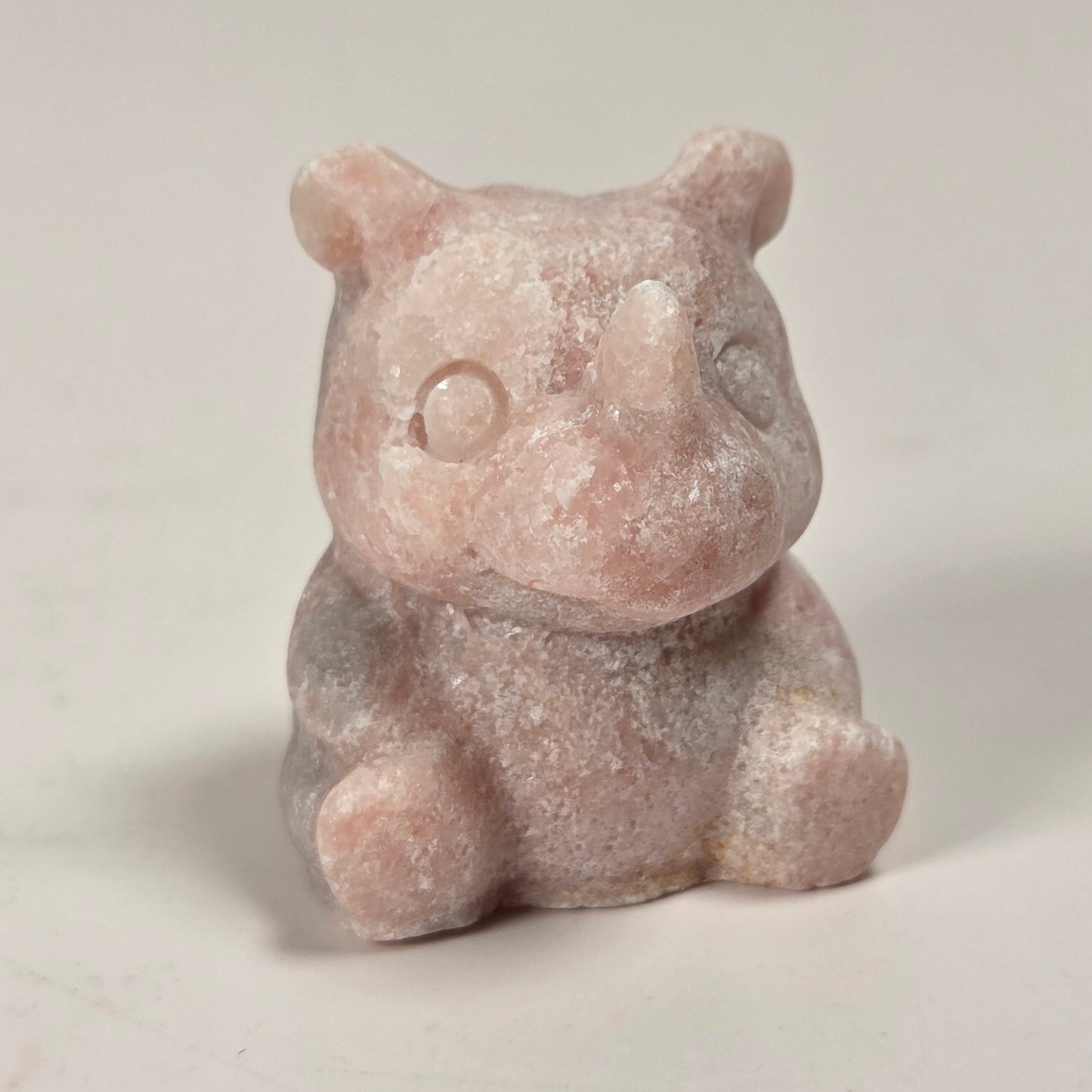 A small pinkish stone figurine of a seated bear or pig, photographed on a plain light background.