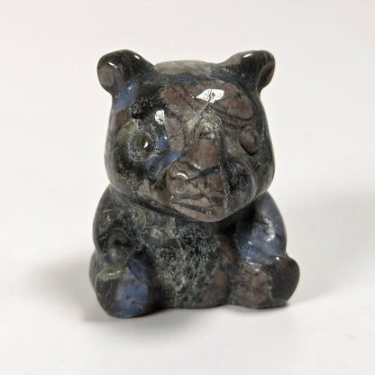 A small carved figurine of a bear, made from polished labradorite stone with natural blue, gray, and brown inclusions, set against a plain white background.