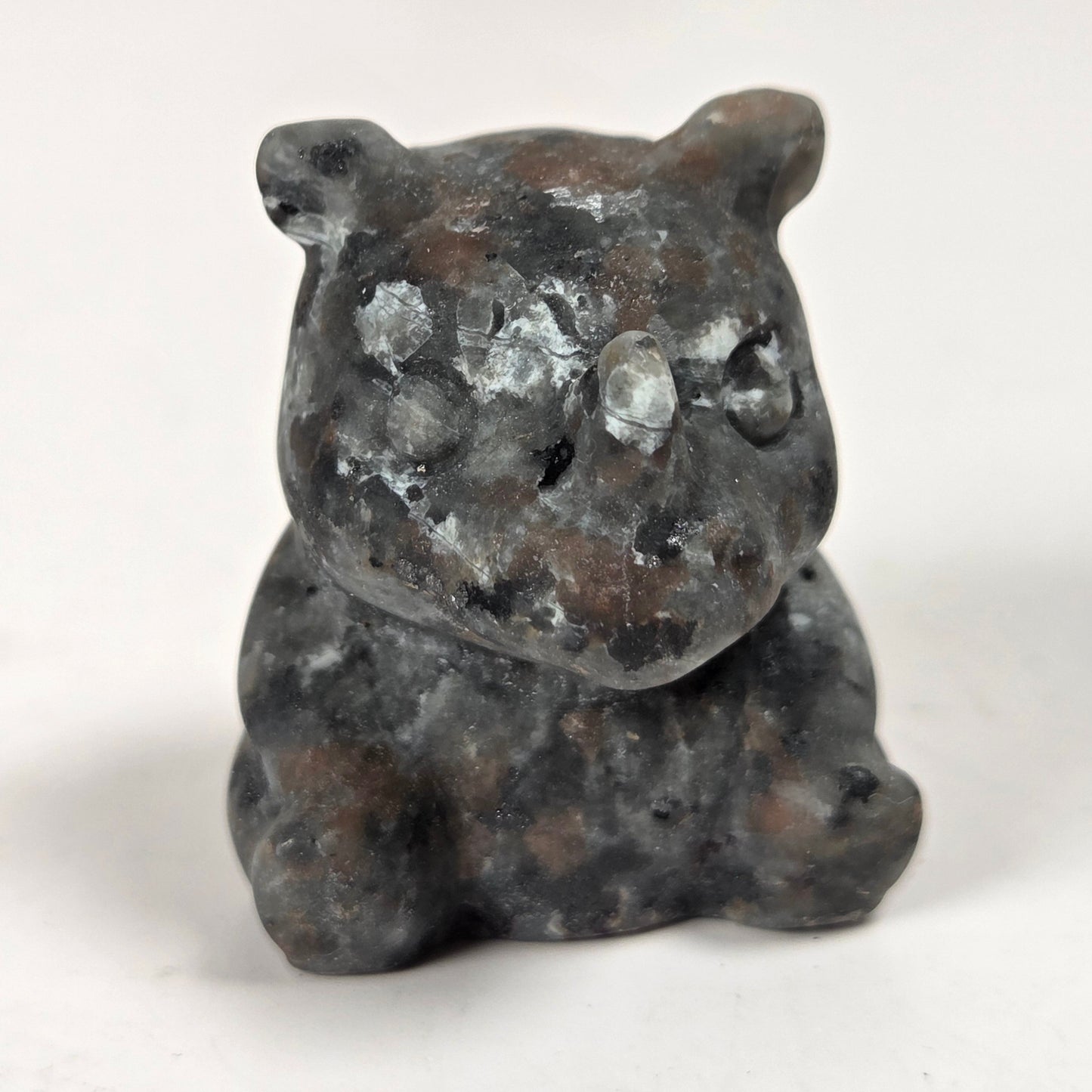 A small carved stone figurine of a bear, made from dark gray and brown natural stone with white marbled patches, set against a plain white background.