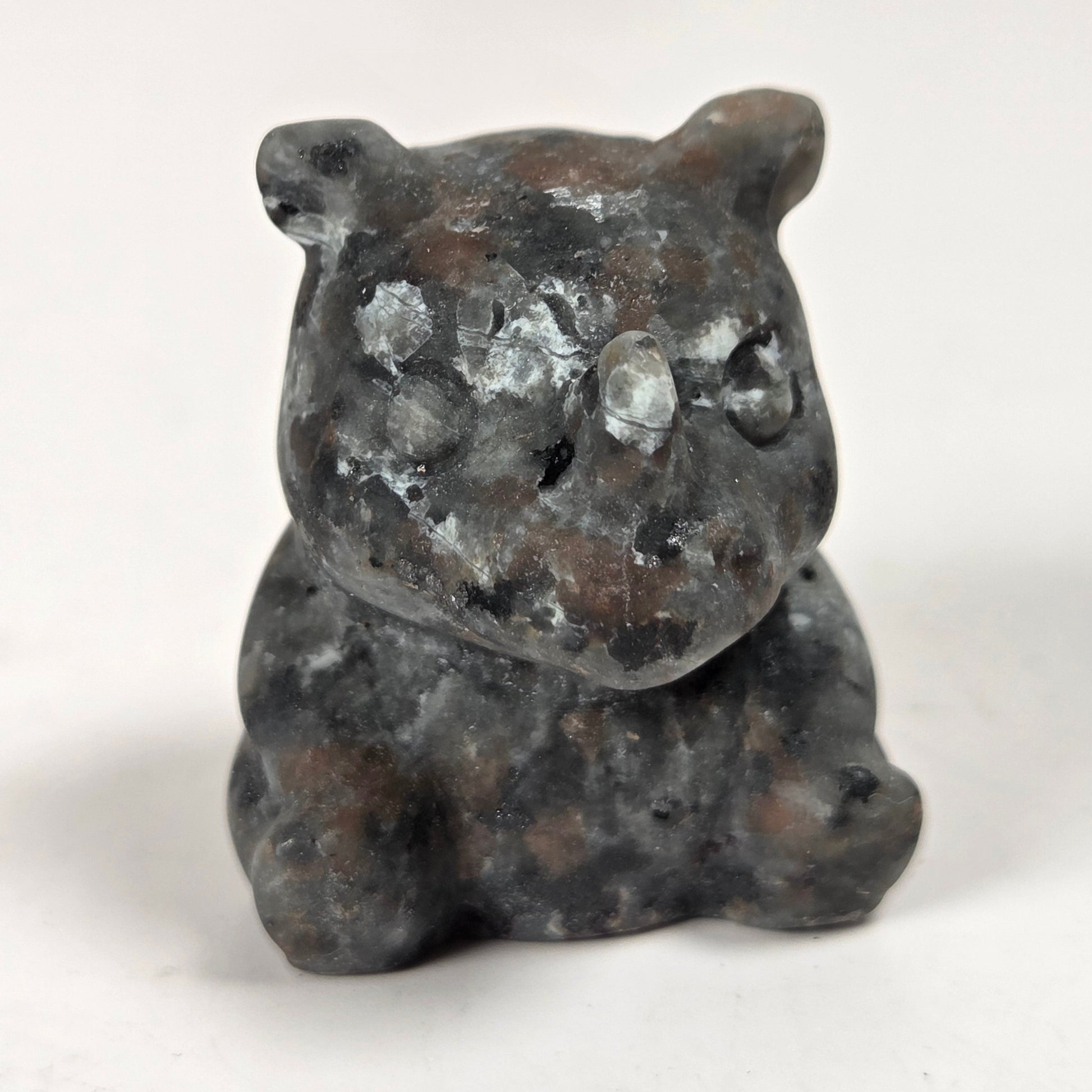 A small carved stone figurine of a bear, made from dark gray and brown natural stone with white marbled patches, set against a plain white background.