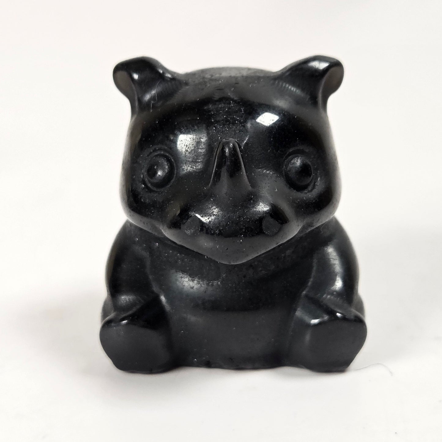 A small glossy black figurine shaped like a seated animal or creature, photographed against a plain white background.