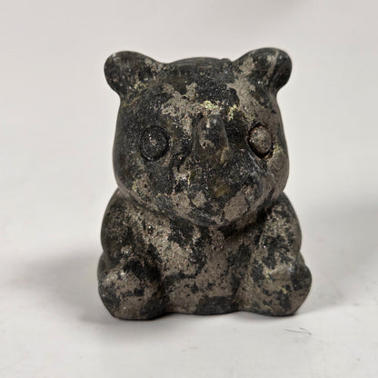 A small carved figurine of a seated animal, likely a bear or cat, made from dark stone with a mottled gray and black texture, photographed on a plain light background.