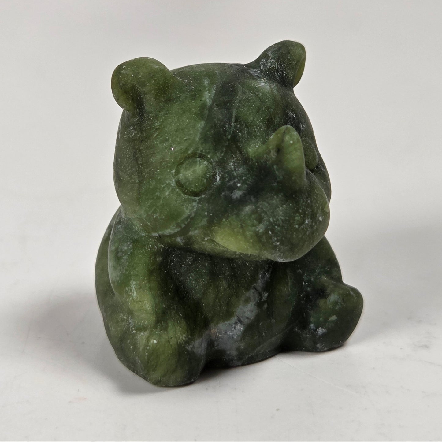 A small carved green stone rhinoceros figurine sitting on a light gray surface.
