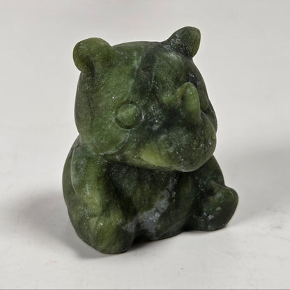 A small carved green stone rhinoceros figurine sitting on a light gray surface.