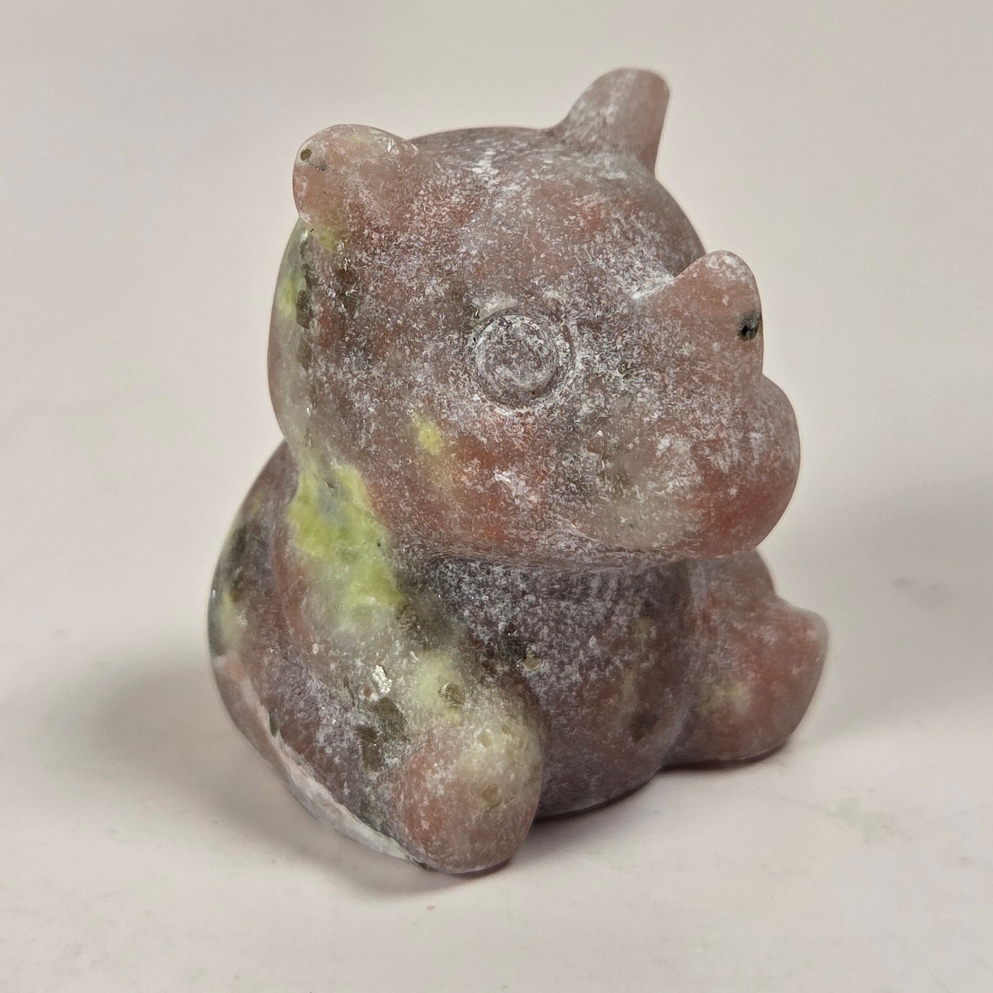 A small carved figurine of a seated animal, likely a pig or boar, made from a pinkish stone with green and gray marbling, photographed on a plain light background.