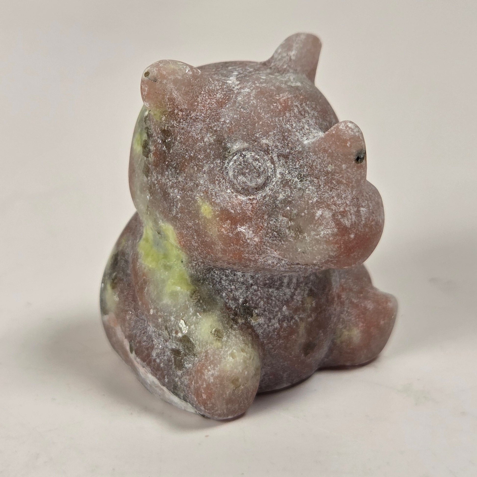 A small carved figurine of a seated animal, likely a pig or boar, made from a pinkish stone with green and gray marbling, photographed on a plain light background.