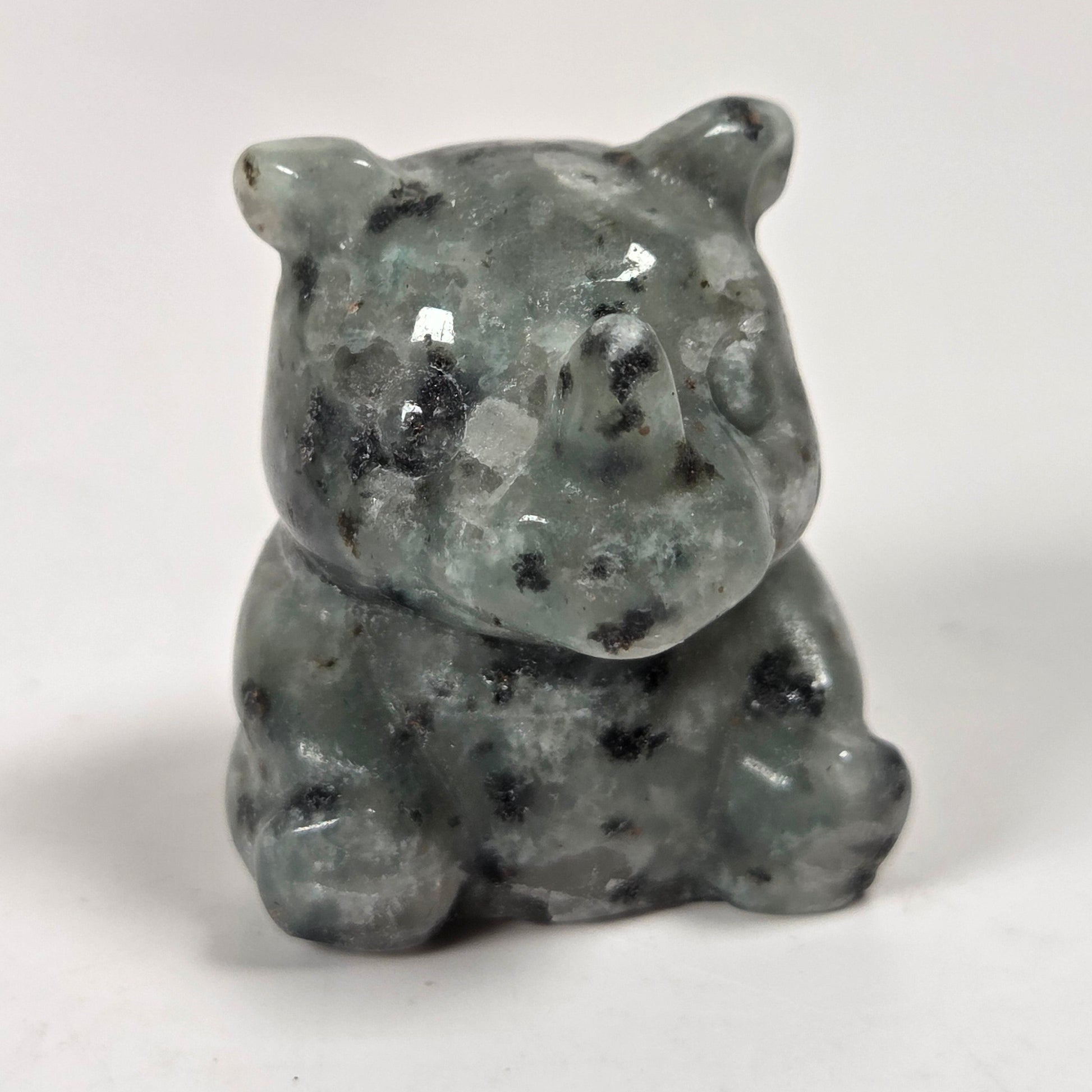 A small carved stone figurine of a bear, made from gray-green mottled stone with black inclusions, set against a plain light gray background.