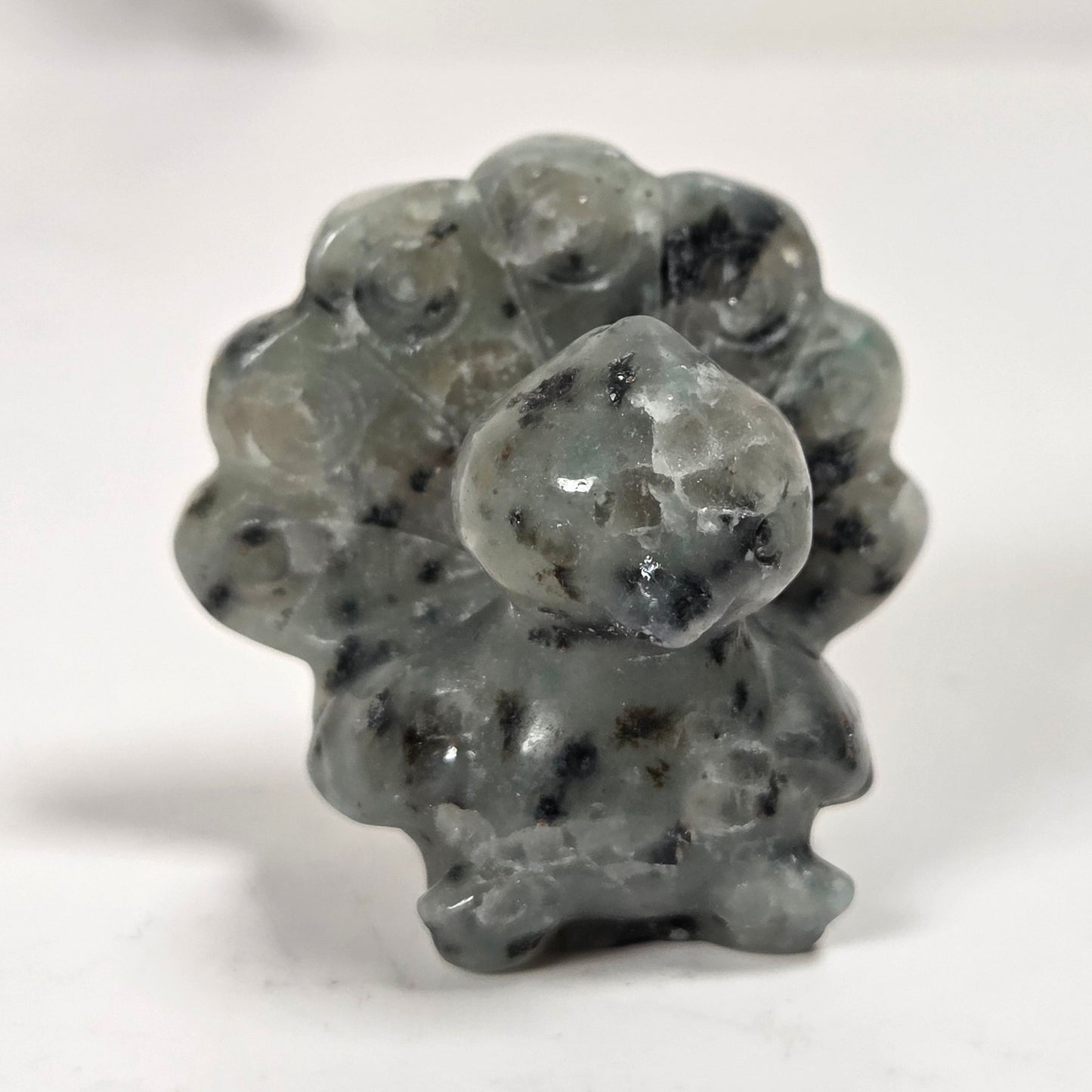 A small carved stone figurine with a textured, speckled appearance in gray and black, standing on a plain white surface.