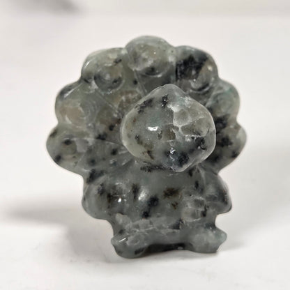 A small carved stone figurine with a textured, speckled appearance in gray and black, standing on a plain white surface.