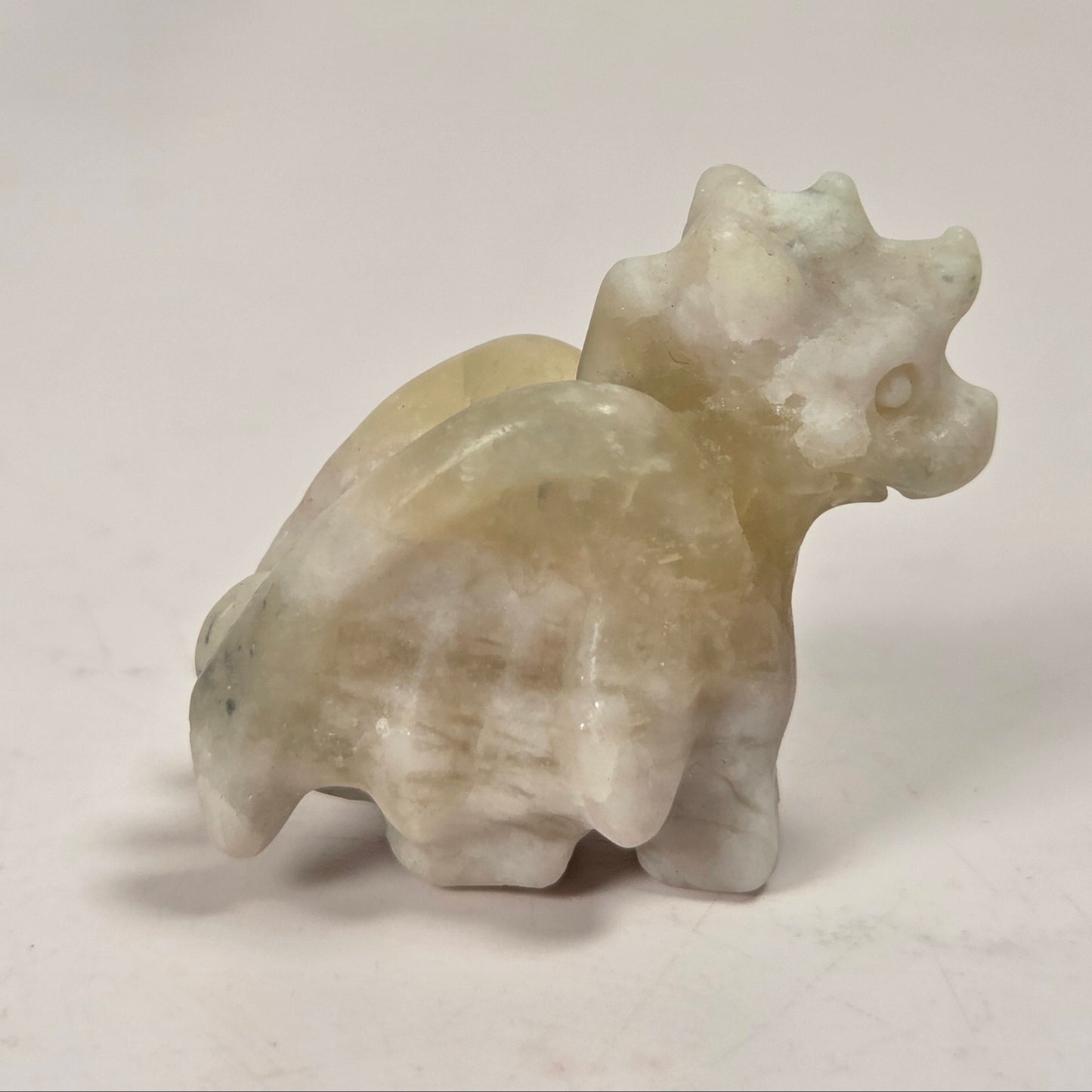 A small carved stone figurine of a horned animal, likely a bull or ox, in pale cream, beige, and light green marbled stone, standing on a plain light background.