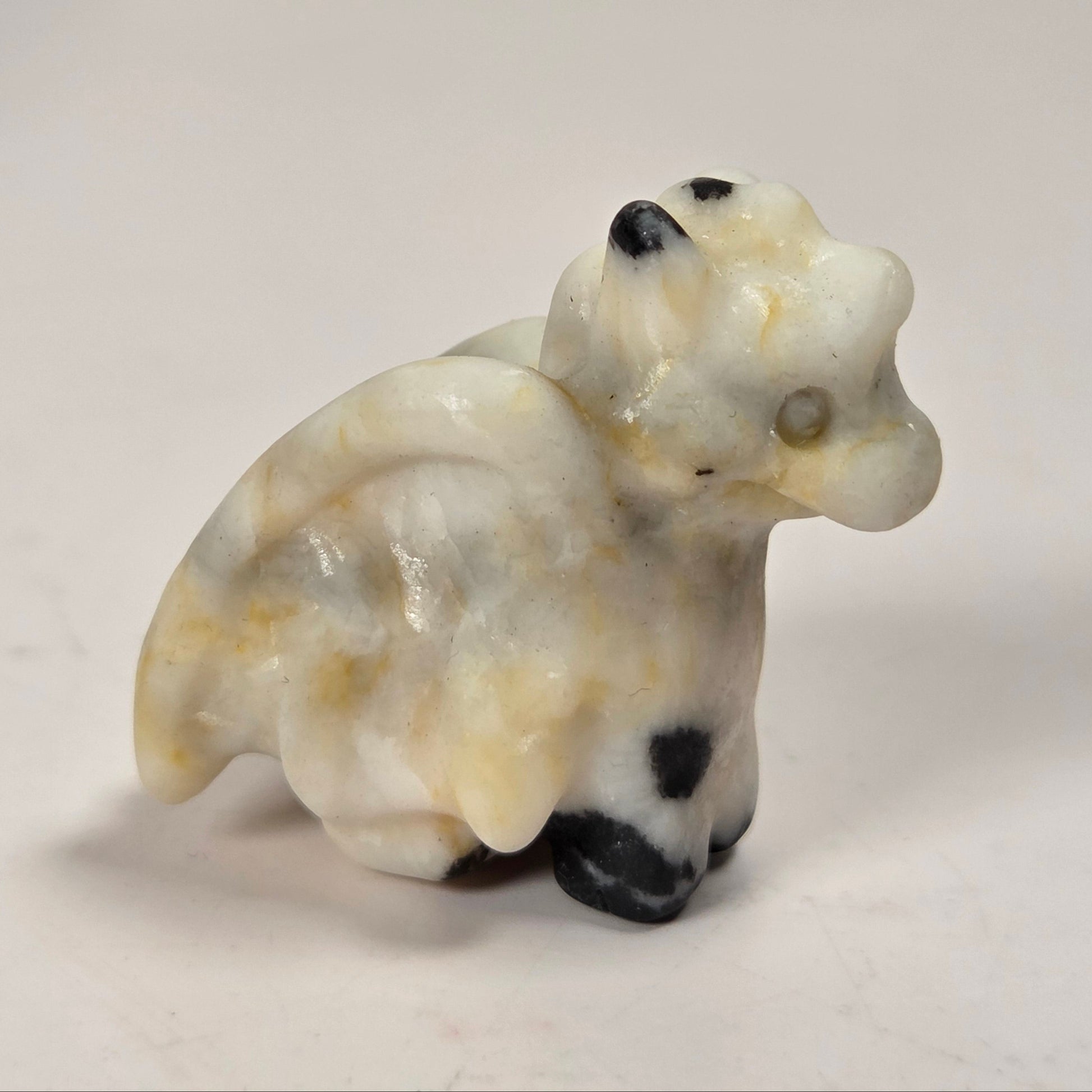 A small carved figurine of a cow or bull made from marbled stone, featuring cream, beige, and white tones with black and dark brown accents on its face, hooves, and body.