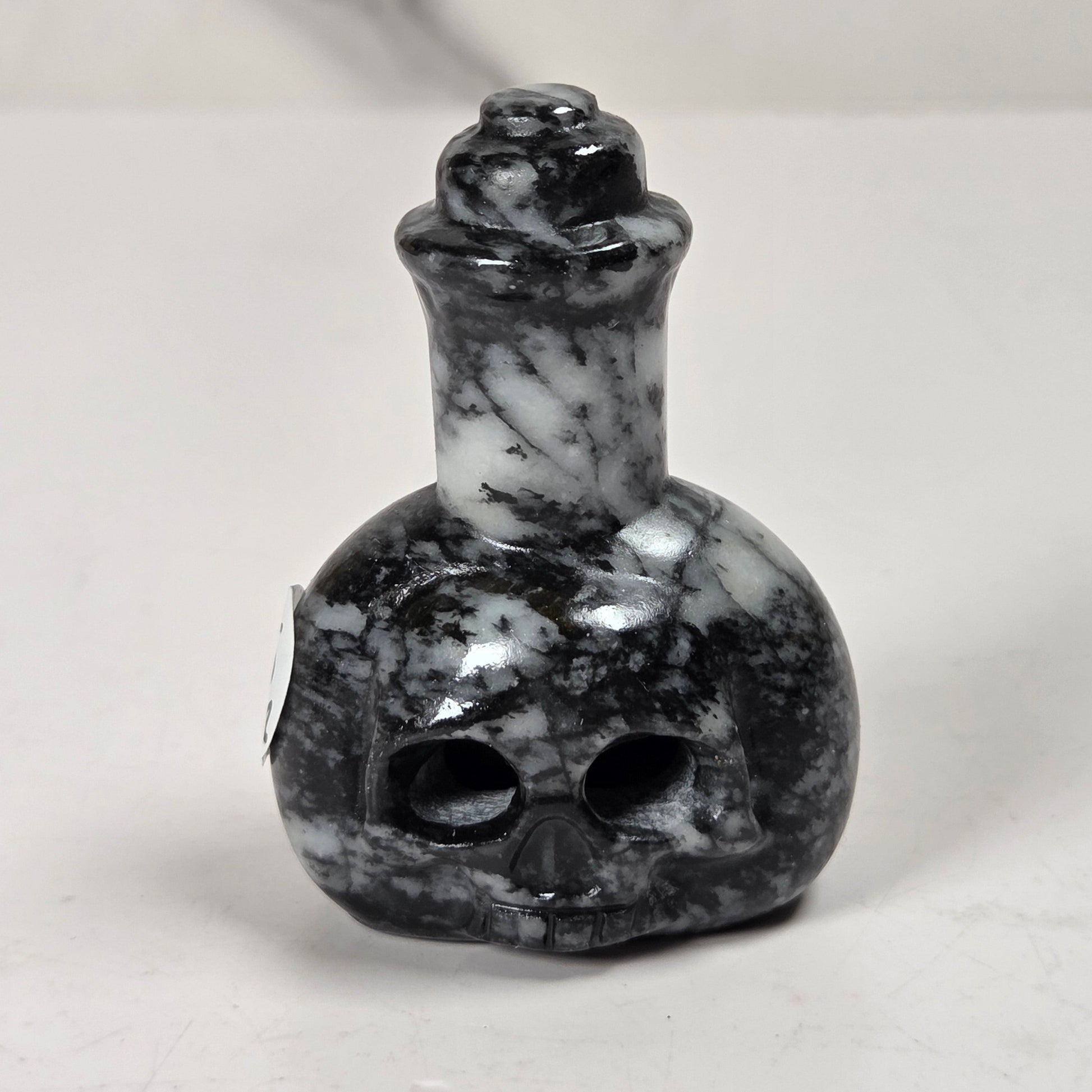 A small carved skull-shaped bottle or perfume bottle made of black and white marbled stone, photographed on a light neutral surface.