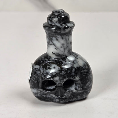 A small carved skull-shaped bottle or perfume bottle made of black and white marbled stone, photographed on a light neutral surface.