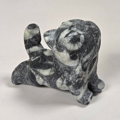 A small carved stone figurine of a cat in a sitting position, made from dark gray and white marbled stone, photographed on a plain light background.