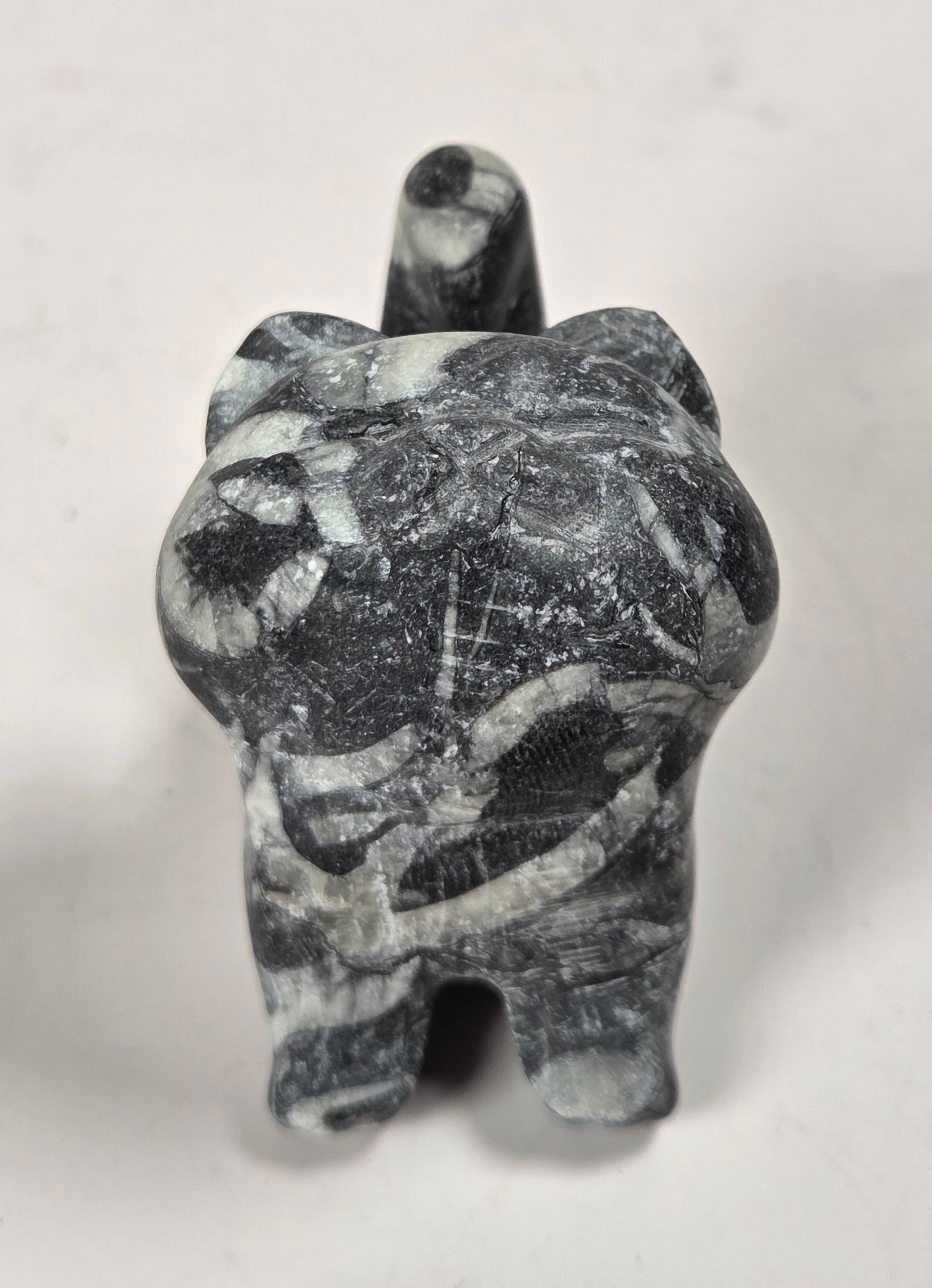 A small carved figurine of a cat made from dark gray and white marbled stone, photographed against a plain off-white background.