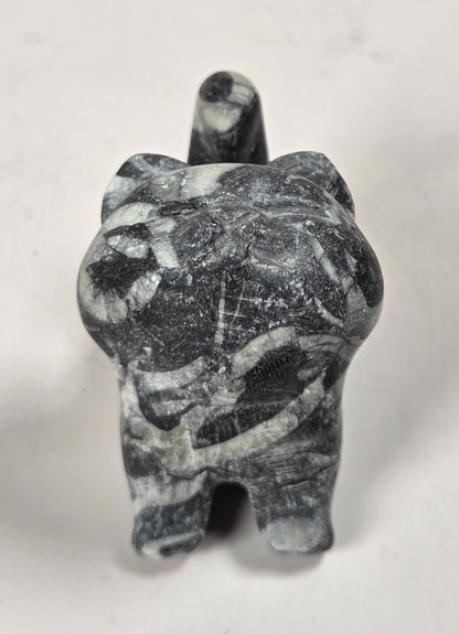 A small carved figurine of a cat made from dark gray and white marbled stone, photographed against a plain off-white background.