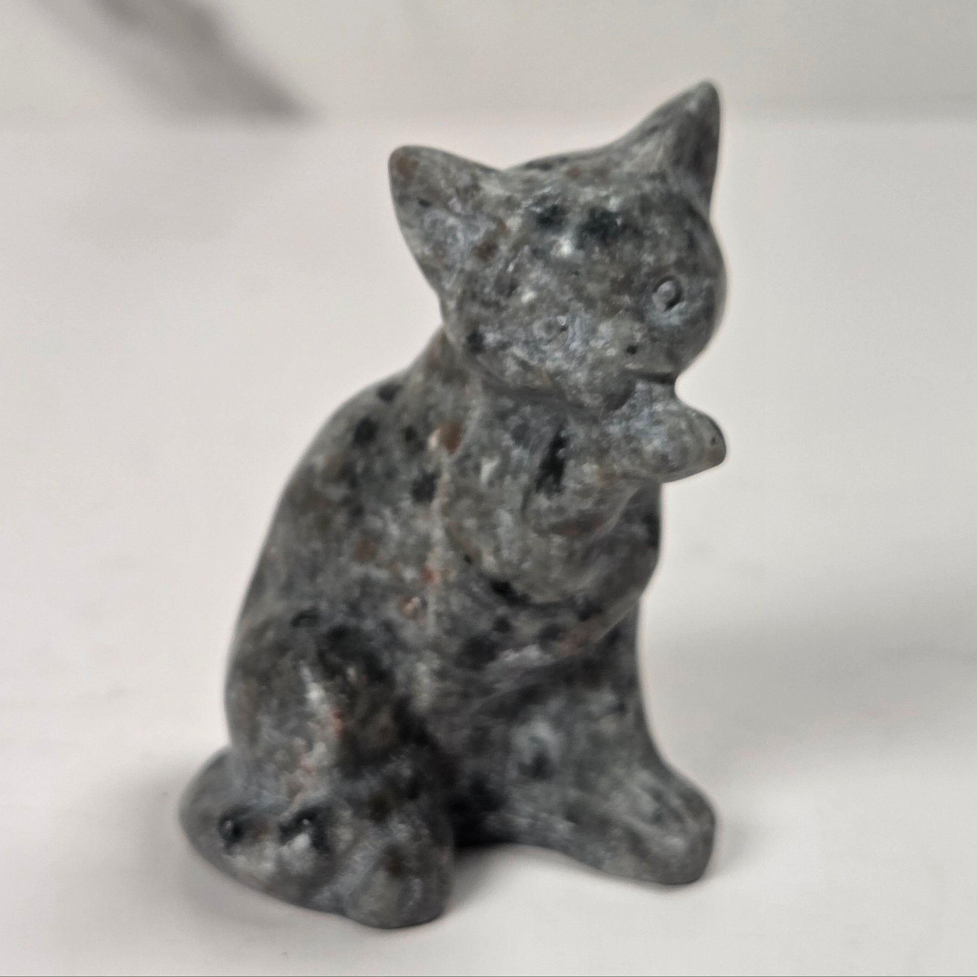 A small gray stone figurine of a cat sitting upright, photographed against a plain light background.