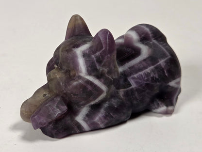 A carved stone figurine of a small cat, made from purple and white marbled stone with a smooth grayish snout, photographed on a plain light background.