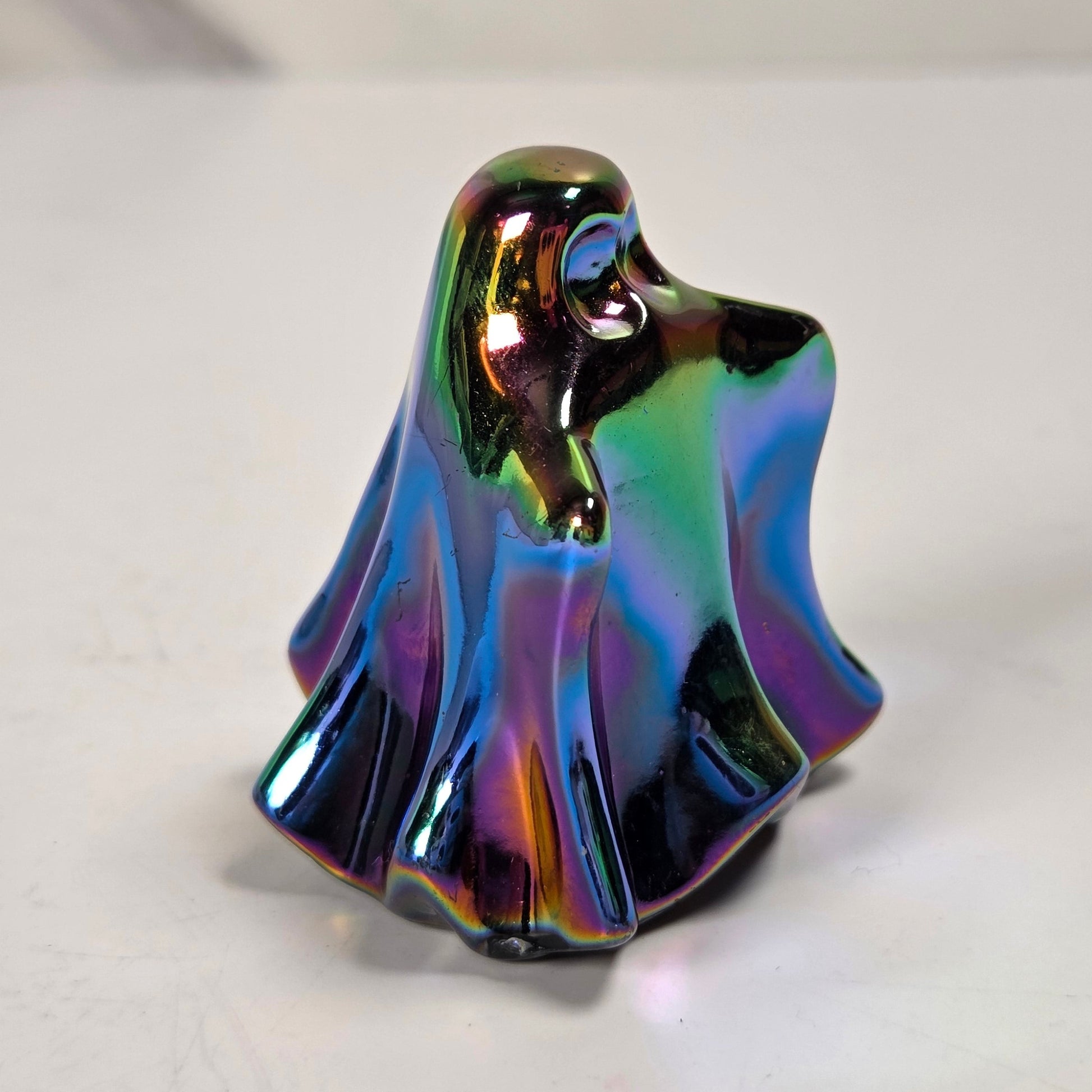 A small glossy ghost-shaped figurine with an iridescent rainbow finish, standing on a light gray surface.