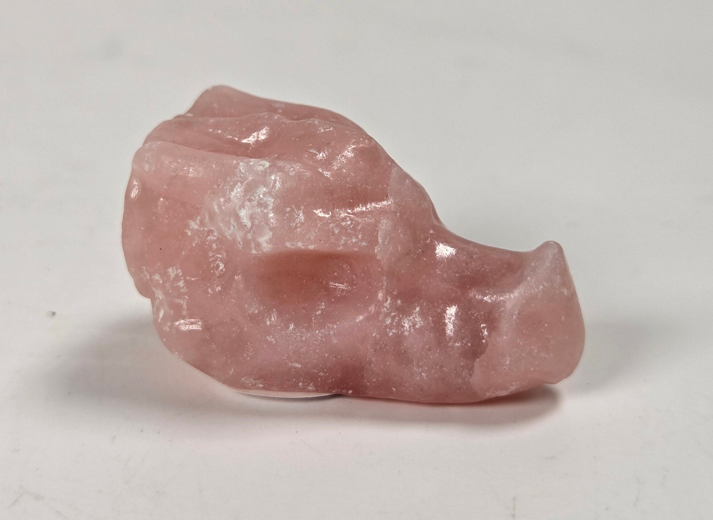 A small polished pink stone carving with a smooth, organic shape, photographed on a plain light gray surface.