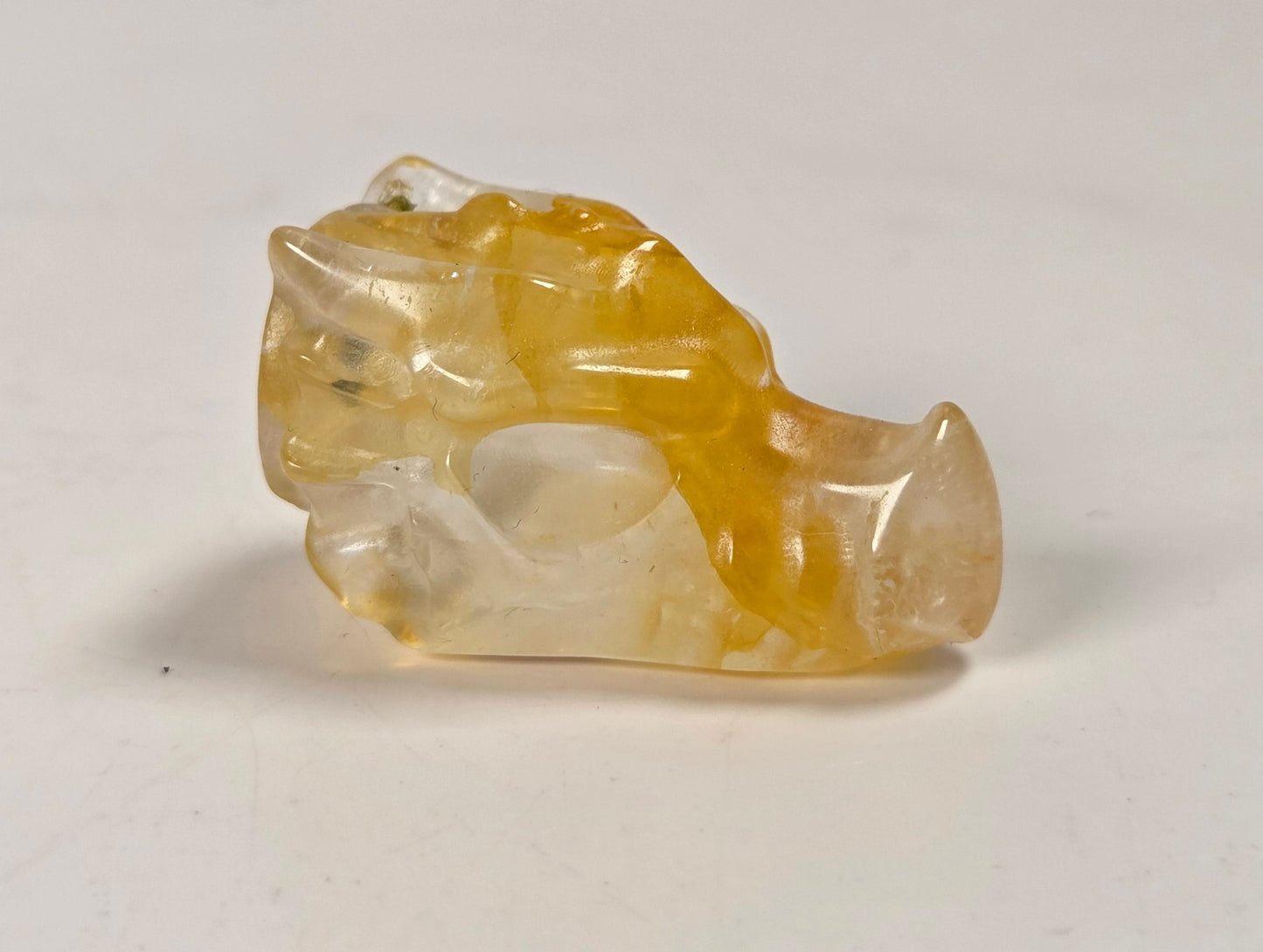 A small carved translucent stone figurine with yellow and white marbling, photographed on a plain off-white surface.