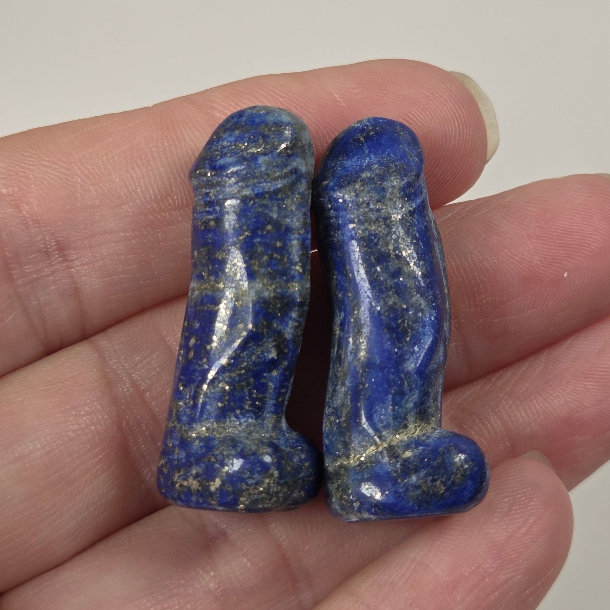 Two small carved lapis lazuli stones with golden flecks, held in a person's hand against a plain light background.