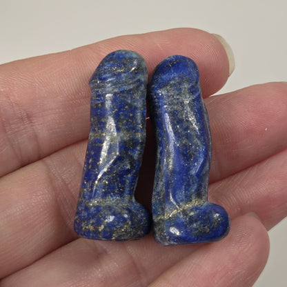 Two small carved lapis lazuli stones with golden flecks, held in a person's hand against a plain light background.
