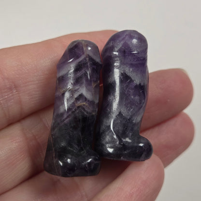 Two small polished purple stone figurines held in a person's hand against a plain light background.