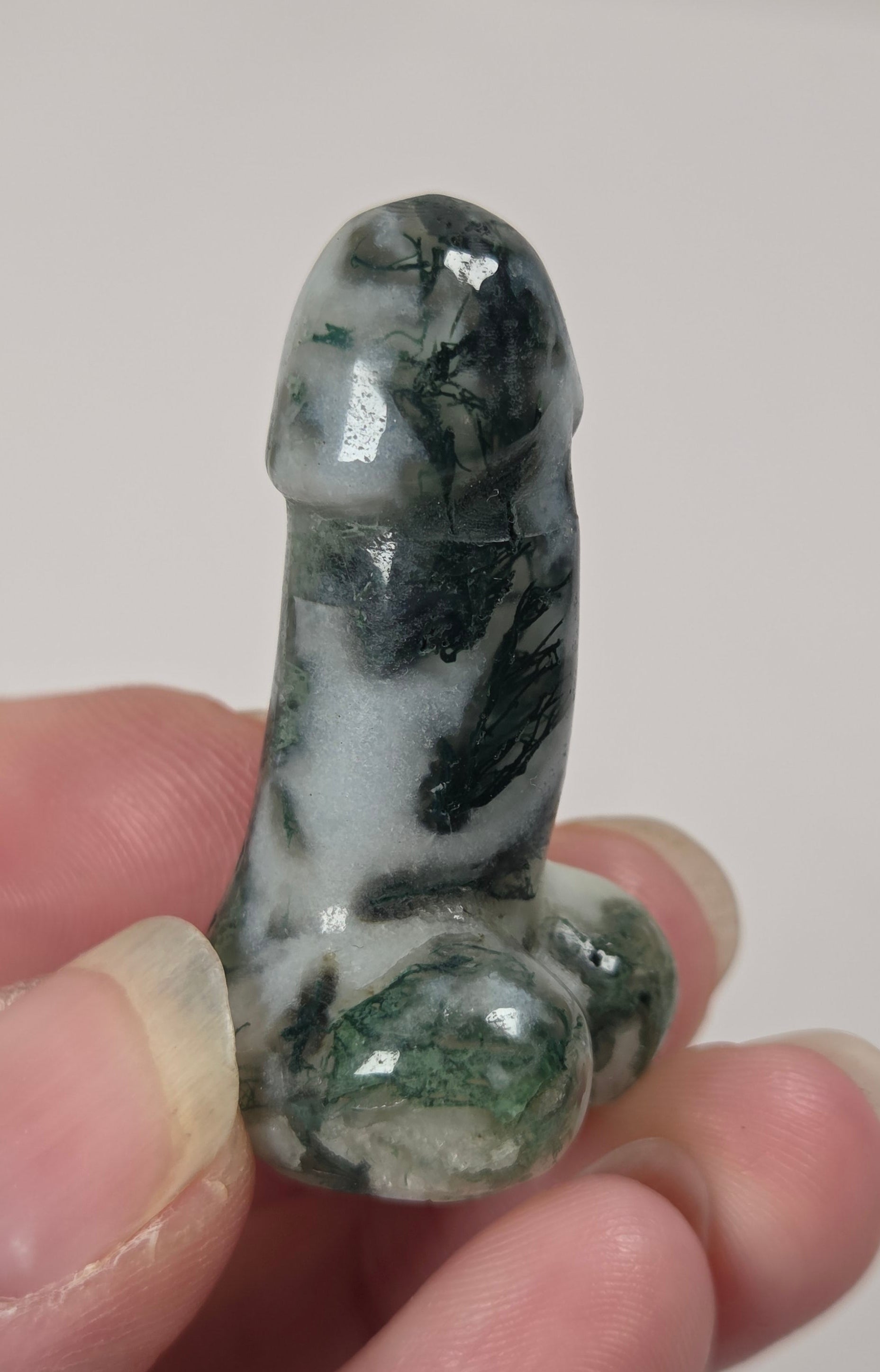 A hand holding a small carved stone figurine with a glossy green and white marbled pattern, photographed against a plain light background.