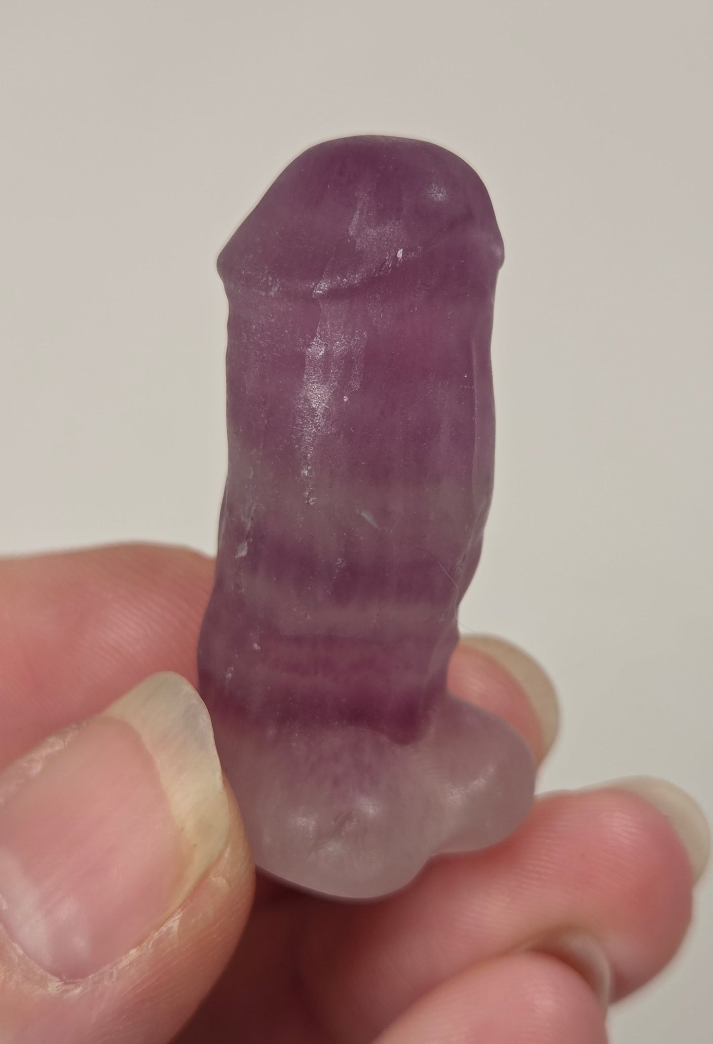 A hand holding a small, polished purple crystal object with a smooth, rounded shape against a plain light background.