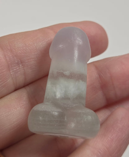 A small translucent pale pink and white stone dildo held in a person's hand against a light gray background.