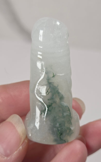 A hand holding a small carved translucent jade-like figurine with green marbling, photographed against a plain light background.