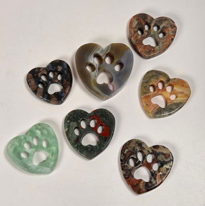 Seven heart-shaped buttons with paw print cutouts, made from various natural stone materials in different colors, arranged on a plain off-white surface.