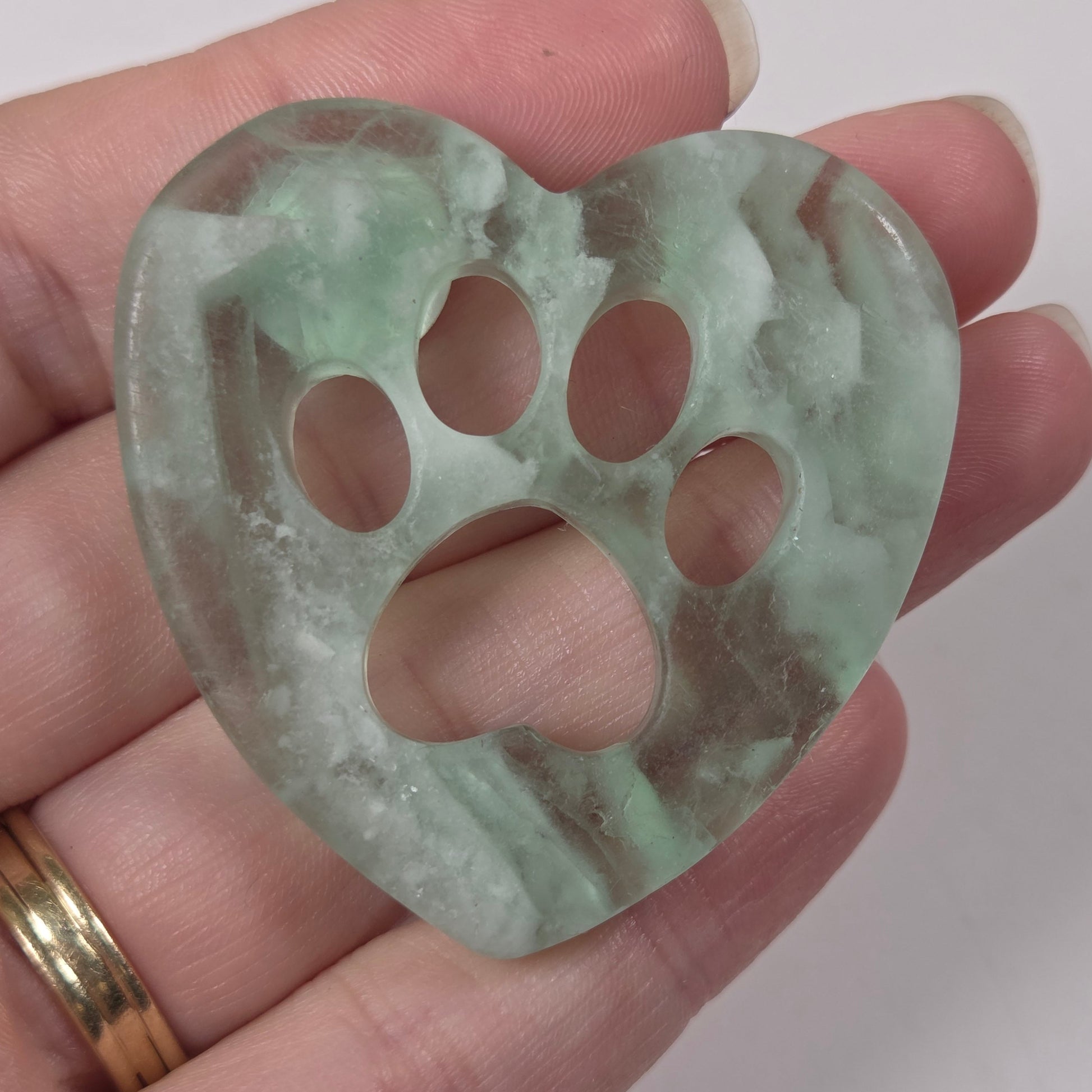 A heart-shaped green stone or jade pendant with a paw print cutout, held in a person's hand against a plain light background.