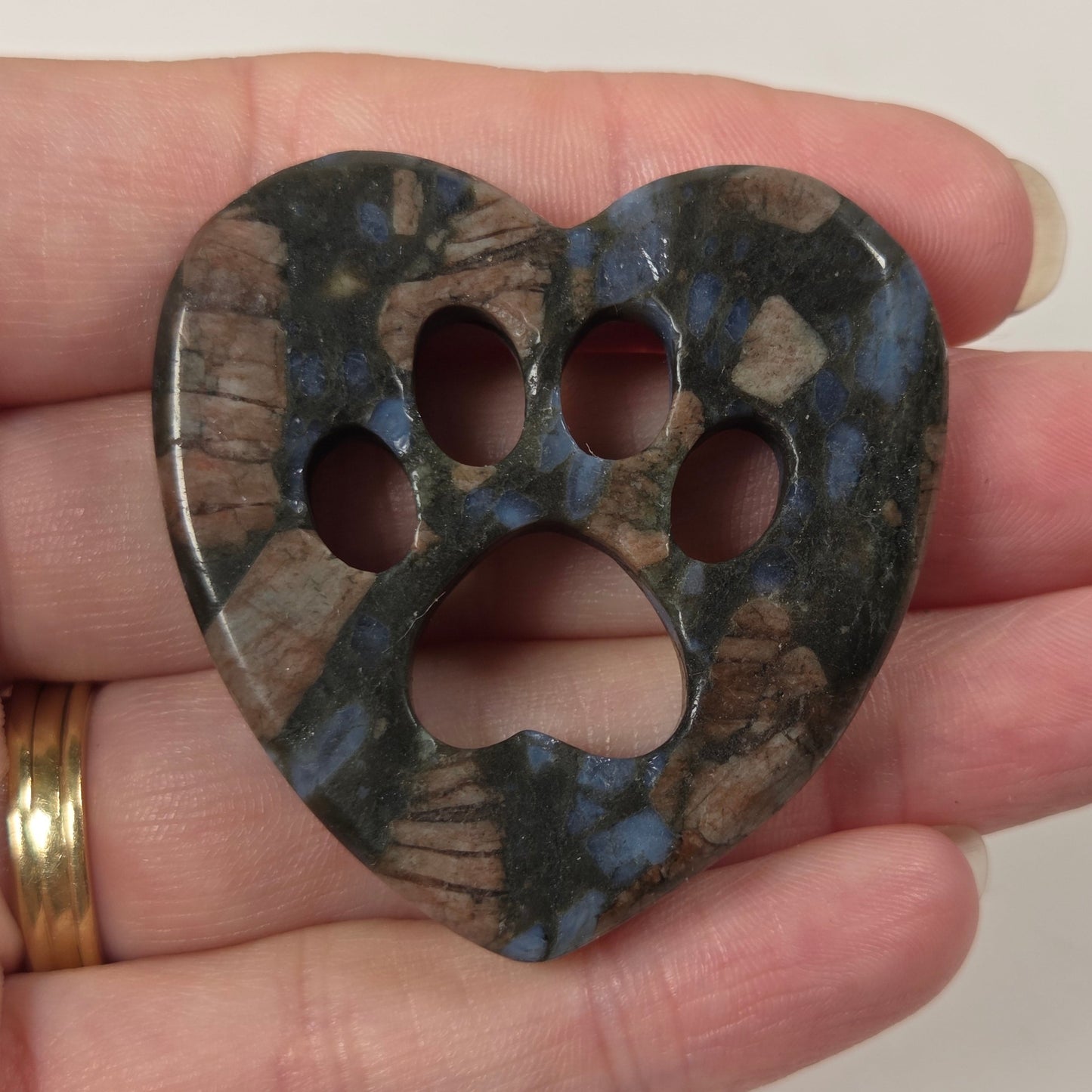 A heart-shaped paw print pendant made of blue and brown marbled stone, held in a person's hand against a plain light background.