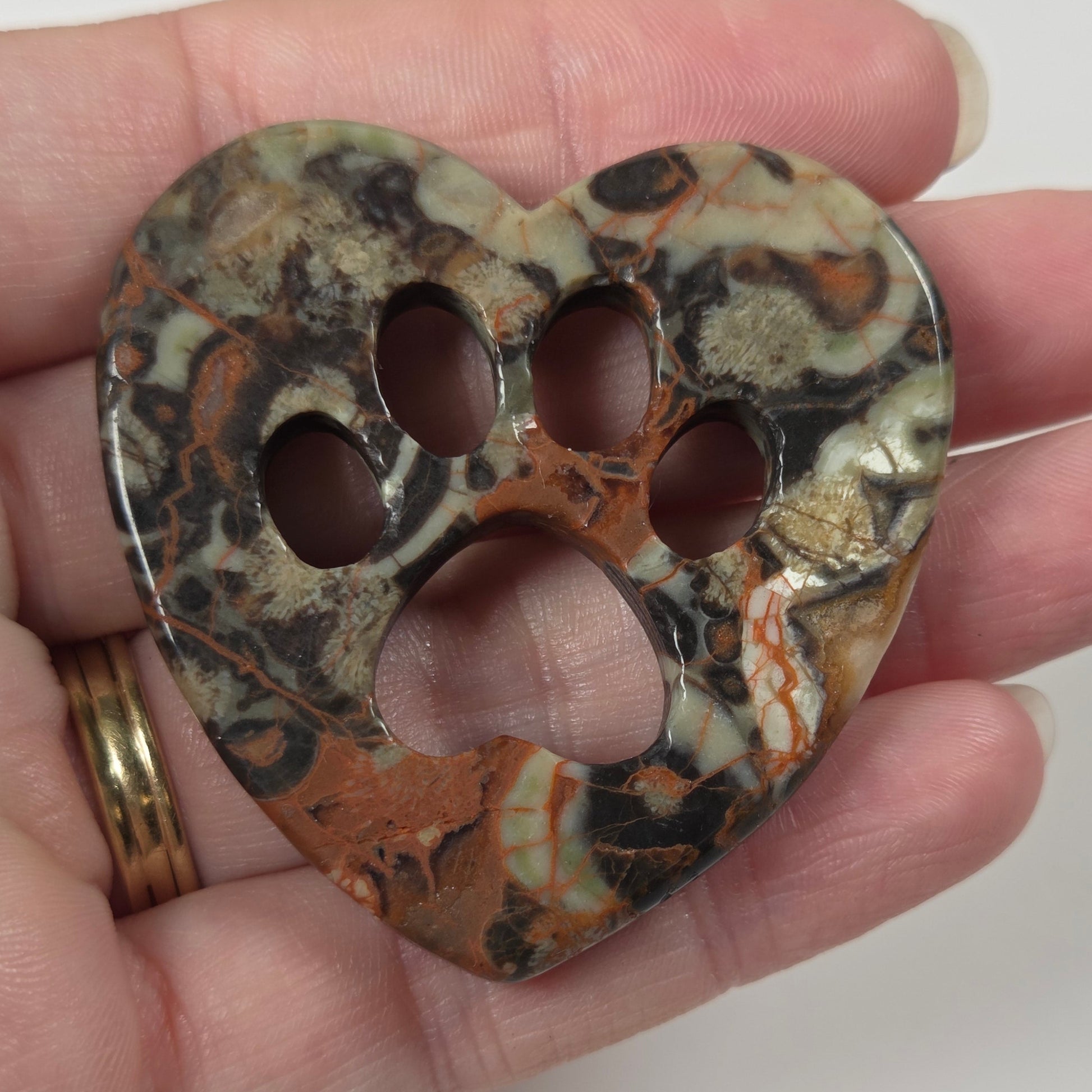 A heart-shaped bone-shaped pendant with a paw print cutout, featuring a marbled pattern of brown, black, beige, and white, held in a person's hand.