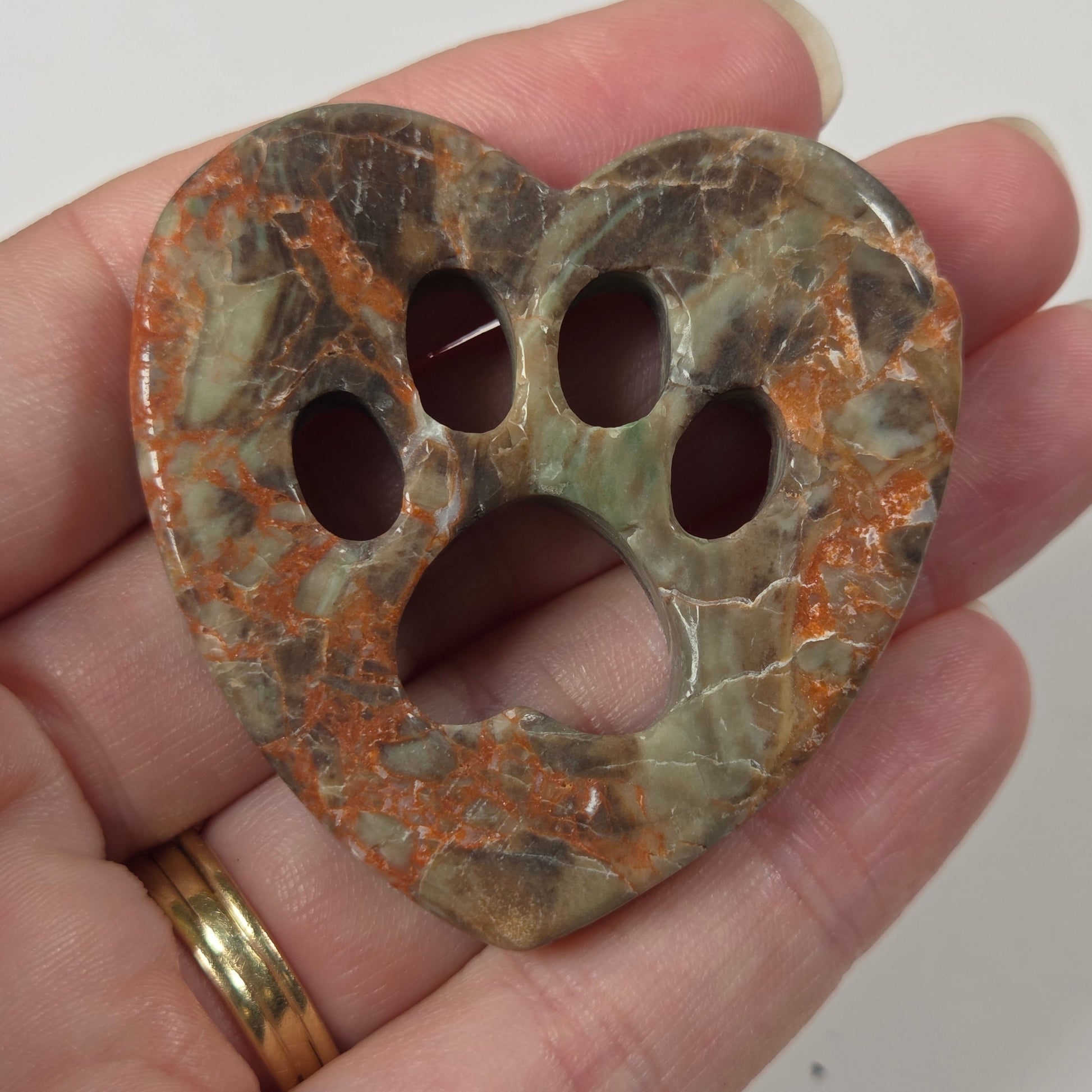 A heart-shaped paw print pendant made of marbled stone with green, brown, and orange patterns, held in a person's hand.