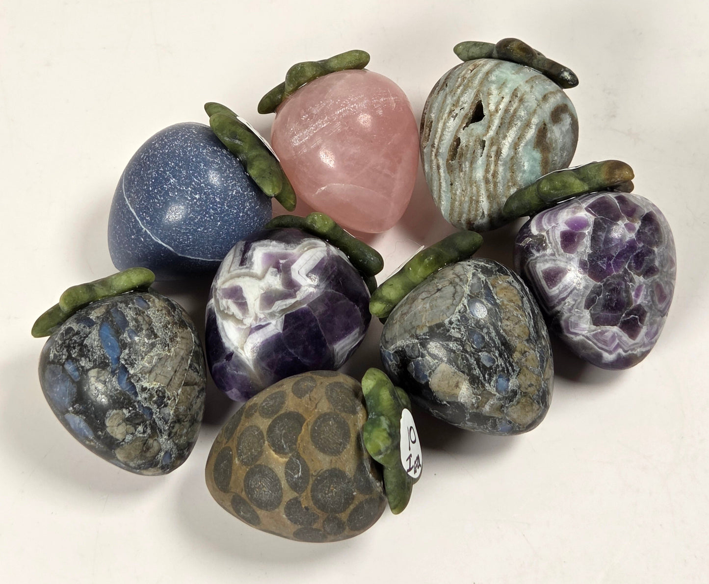A cluster of nine polished gemstone pendants with green moss-like accents, displayed on a plain off-white background.