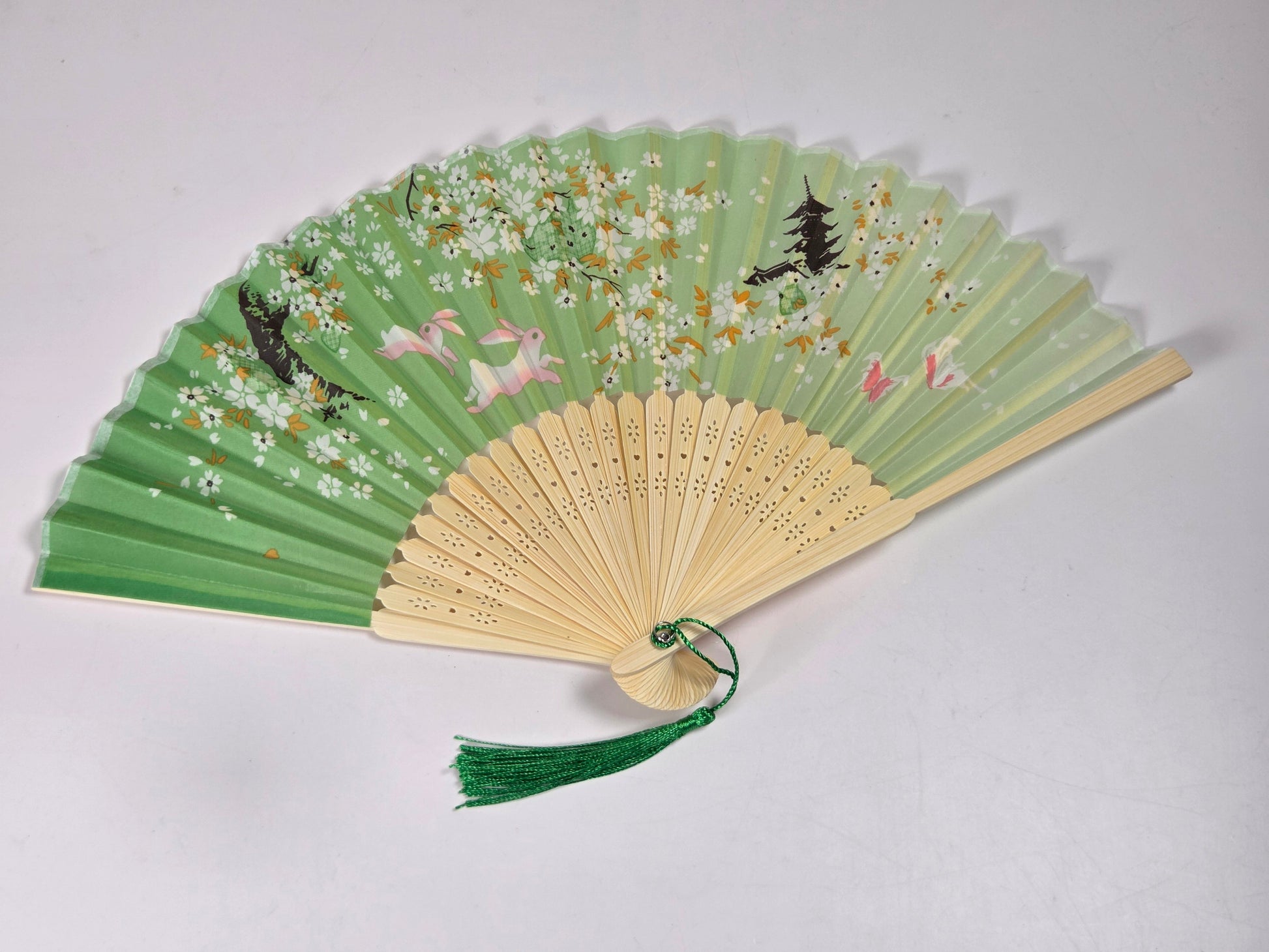 A traditional folding hand fan with a green tassel, featuring a bamboo handle and green paper panels decorated with cherry blossoms, cranes, and birds.