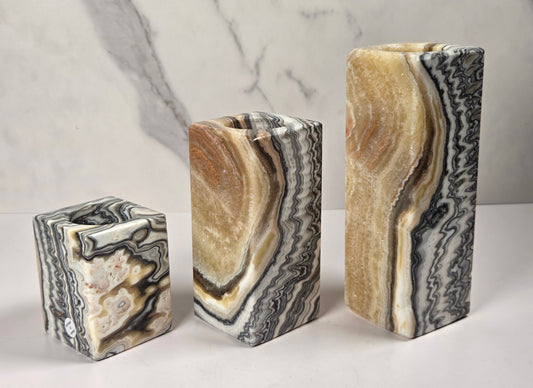 Set of 3 zebra calcite candle holders of varying size with bands of orange, black and white against a white background
