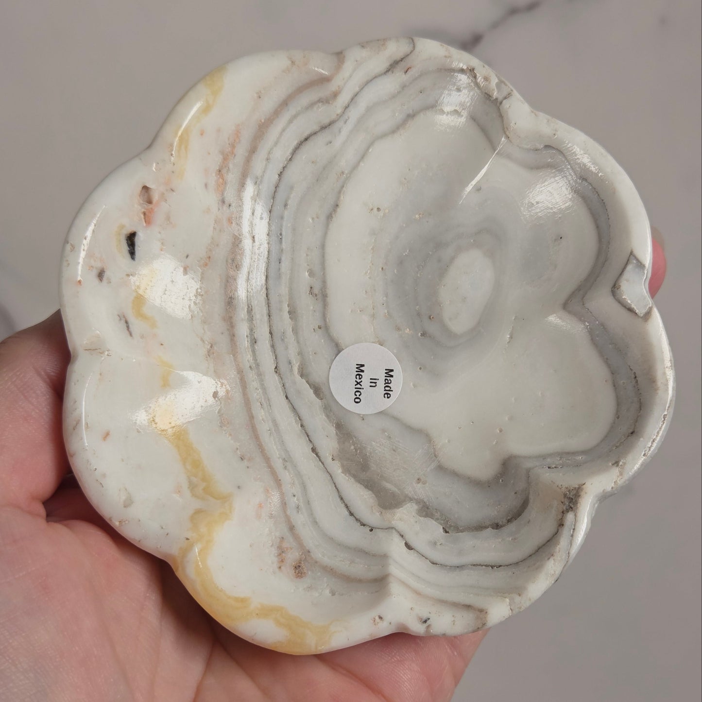 A hand holding a scalloped-edge ceramic plate or shallow dish made from polished agate or marble, showing wavy black, gray, and off-white natural stone patterns.